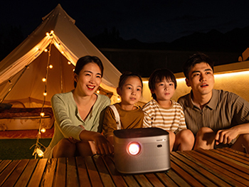 Family outdoors at night in front of a tent watching a movie