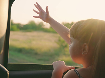 Child holding her hand outside of a moving car