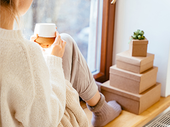 Woman sitting in front of a window in socks with a cup of coffee